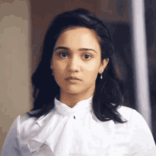 a woman wearing a white shirt and earrings looks at the camera with a serious look on her face