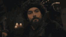 a man with a beard is wearing a fur hat and a black coat .