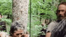 a man is standing next to a tree in the woods .