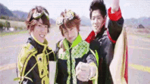 three young men are standing next to each other on a road and pointing at the camera .