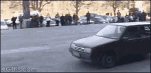 a car is driving down a street in front of a crowd of people and the website 4gifs.com is displayed on the bottom