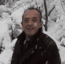 a man in a brown jacket is smiling in front of a snowy forest