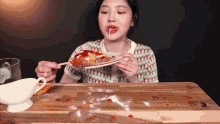 a woman is sitting at a table eating a plate of food with sauce on it