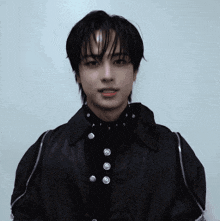 a young man wearing a black jacket with buttons on it looks at the camera
