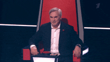 a man in a suit sits in a red chair with the number 7 on the back