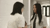 two girls in school uniforms and ties are talking to each other in a hallway
