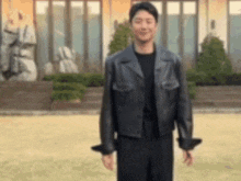 a man wearing a leather jacket is standing in front of a building .