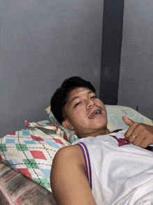 a young man laying on a bed with his tongue hanging out and a jersey that says nike on it