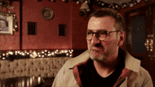 a man wearing glasses and a plaid shirt is sitting in front of a tv screen that says ' itv '