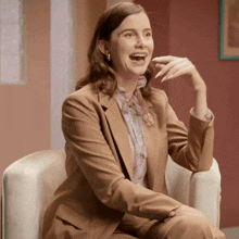 a woman in a tan suit is sitting in a chair and laughing