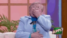 an older woman covering her mouth with her hands and a sign that says apm behind her