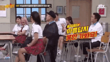 a group of people are sitting at desks in a classroom with a sign that says jtbc on it .