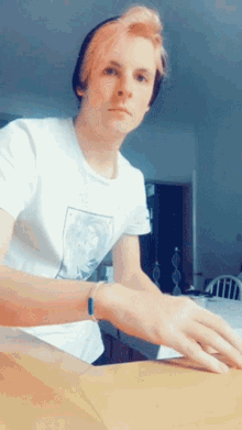 a young man with pink hair is wearing a white shirt and a black hat