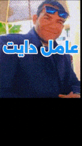 a man wearing sunglasses and a blue jacket has arabic writing on his face