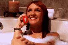 a woman in a bathtub talking on a cell phone with a candle in the background