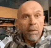 a bald man with a beard is making a funny face while wearing a hoodie .