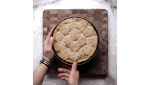 a person is holding a cookie in a pan on a wooden cutting board .