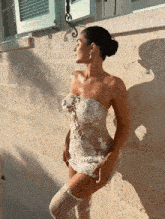 a woman in a white lace dress stands in front of a brick wall