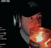 a man wearing headphones and a trash hat holds a burning candle