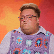 a man wearing glasses and a purple sweater vest