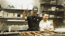 a man in a chef hat stands next to another man in a white shirt