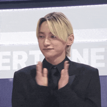 a man in a black suit applauds in front of a screen that says ert ne