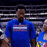 a man with a beard wearing a los angeles basketball shirt is being interviewed by a woman .