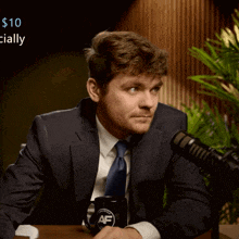 a man in a suit and tie sitting in front of a microphone with a mug that says af