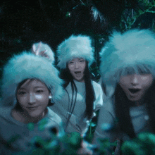 three women wearing furry hats are standing in a forest