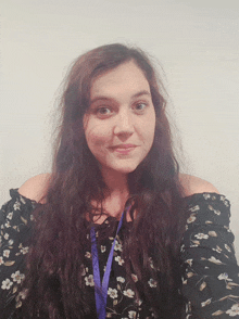a woman with long hair is wearing a black floral shirt and a purple lanyard around her neck