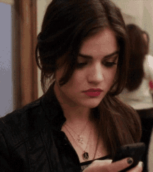 a woman wearing a leather jacket and a necklace with a star on it looks at her phone
