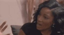 a woman in a black shirt is sitting on a couch and talking to someone .