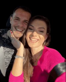 a man and woman are posing for a picture and the woman is wearing a bright pink sweater