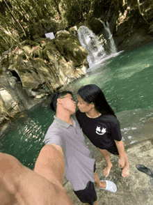 a man kissing a woman in front of a waterfall
