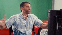 a man in a hawaiian shirt is sitting in front of a computer monitor