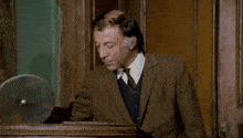 a man in a suit stands next to another man in a barrel