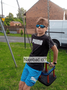 a boy wearing sunglasses and a puma shirt sits on a swing set