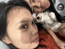 two women are laying on a bed with a small white dog between them