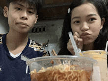 a boy and a girl are sitting next to each other eating noodles