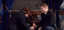 two men are sitting next to each other and one of them is holding the other 's hand and saying yeah .