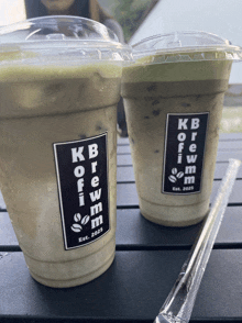 two cups of kb brew are on a table with straws