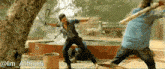 a man in a blue shirt is fighting another man with a stick in a scene from a movie titled @lm_alhindi