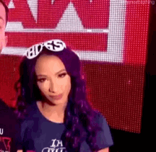a woman with purple hair is wearing a blue shirt and a headband with the word boss on it .