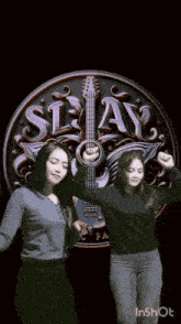 two women are dancing in front of a logo for slay