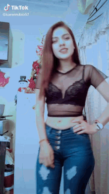 a woman wearing a black crop top and blue jeans stands in a kitchen