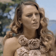 a woman wearing a necklace of roses looks at the camera