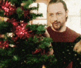 a man standing next to a christmas tree with red decorations