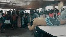 a man is laying on the hood of a car in front of a crowd of people with toms 2005 written on the bottom