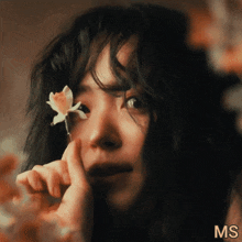 a close up of a woman holding a flower in front of her eye with the letters ms above her