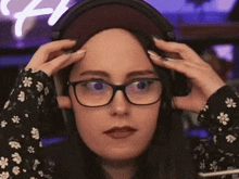 a woman wearing headphones and glasses is holding her head .